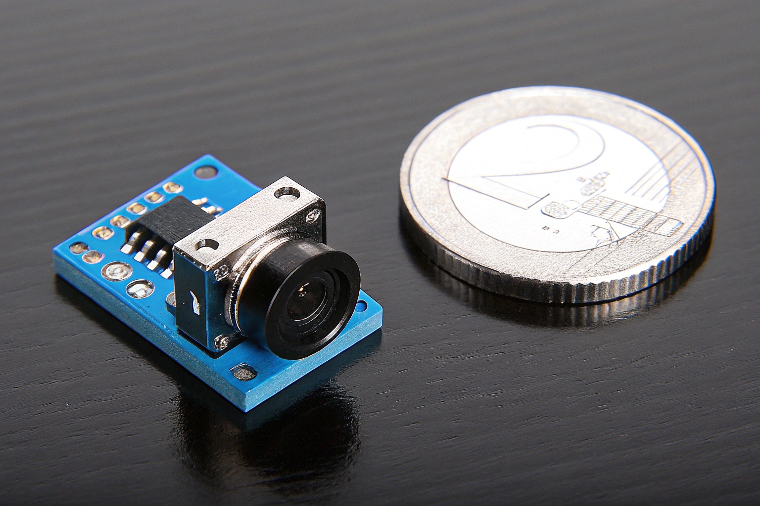 A tiny spy camera module next to a one euro coin for scale